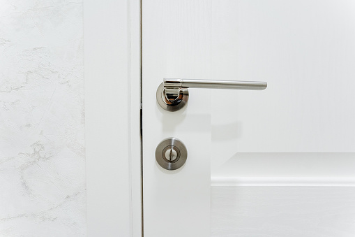 Silver door handle, furniture hardware, door locking mechanism, closed door to the room. High quality photo
