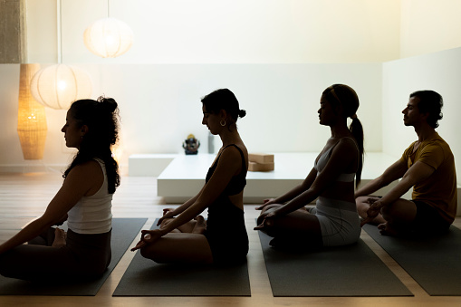 Silhouettes of a yoga class in meditation pose against a softly lit background, evoking calm