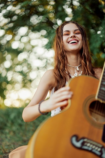 A young hippie woman with a guitar in her hands smiles sweetly into the camera on a trip to nature lifestyle in harmony. High quality photo