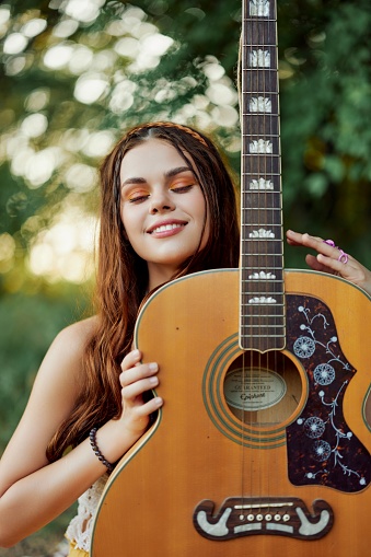 A young hippie woman with a guitar in her hands smiles sweetly into the camera on a trip to nature lifestyle in harmony. High quality photo