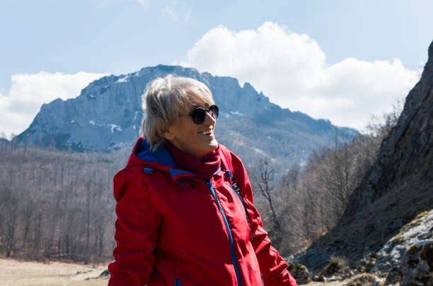 Senior woman in red jacket escape from the city bustle and walk on mountain during a spring day.  Relaxing in nature -care of health. Happy woman in the mountain. Facial expression