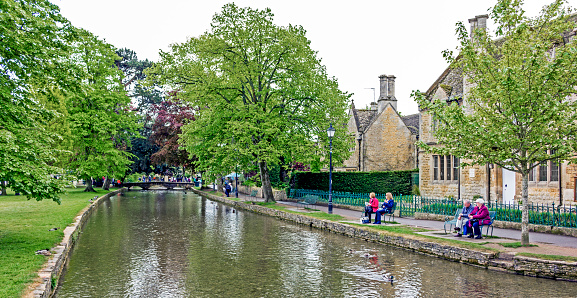 View across the River Windrush at Bourton-on-the-Water, UK.  People can be seen sitting on benches