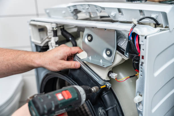 istock Washing machine repair. Repairman uses a electric screwdriver  disassembles a washing machine for repair 2148940419