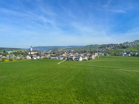 A scenery of of countryside nature of Switzerland and bleu sky, cloud with green grass trees and nature with houses of the village during sunny spring season