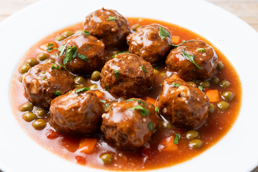 Meatballs, green peas and carrot with tomato sauce isolated on white background on wooden table