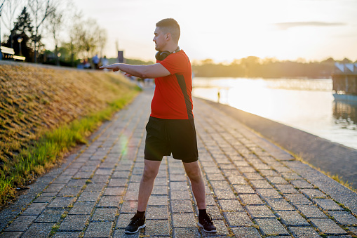 The riverbank serves as natures gym for a mid-adult man, where his stretching exercises harness the serene setting to boost his physical health and mental well-being