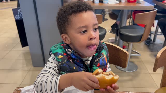 Black toddler, 3.y.o eating a burguer. Handheld camera, unfocused background.