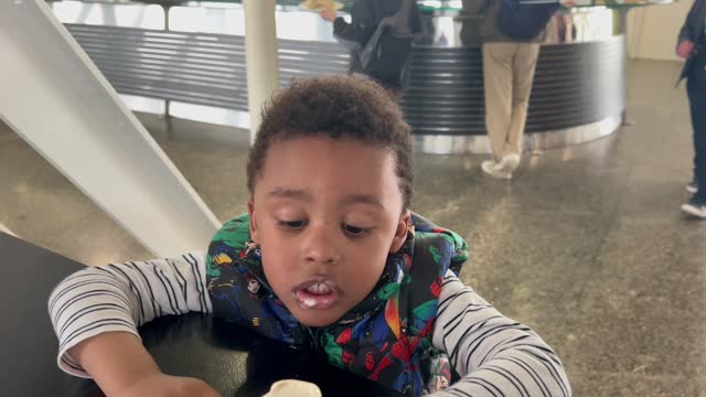 Sweet black child enjoying a melting ice cream inside a cafeteria sitting at the table. 4K