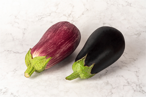 Horizontal photograph of a pair of eggplants of different colors isolated on a marbled white background