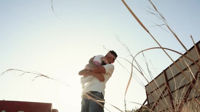 Slow-motion video of a hug of a laughing little child and a man's father in the rays of the setting sun with backlight. Romantic positive spending time a happy family. Trust and support
