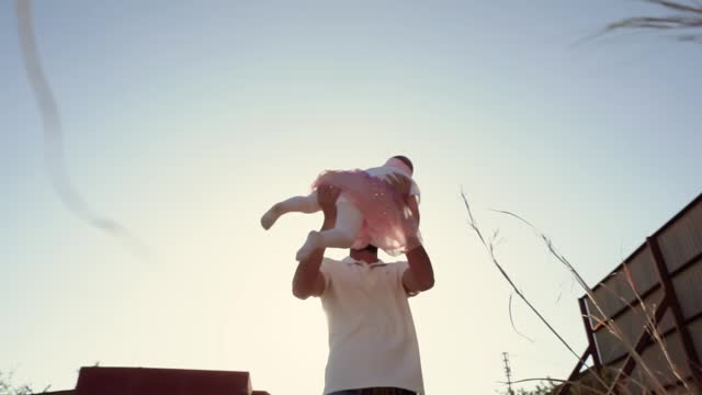 Dad spins his laughing little child daughter around him in the rays of the setting sun with backlight, romantic video of a happy family and parents and children spending time