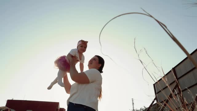 A young woman mother circles her laughing little daughter in the rays of the setting sun with backlight, romantic video of a happy family, parents and children spending time. Trust and support