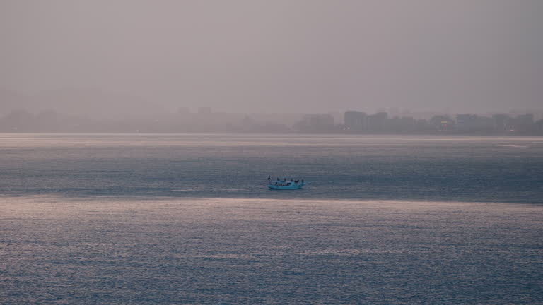 Boat going forward in the middle of the sea with the city in the background on the sea at sunset.