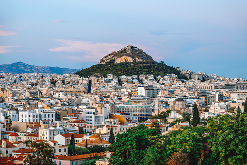 Cityscape view of Athens, Greece, under the brilliance of a sunny summer day, with the iconic Mount Lycabettus towering over downtown. From this vantage point, the city sprawls out beneath the hill, showcasing a blend of ancient and modern architecture. Lycabettus Hill stands as a timeless sentinel, offering a stunning backdrop to the vibrant urban landscape. As the sunlight bathes the scene in warmth, immerse yourself in the beauty of Athens and the commanding presence of Mount Lycabettus, capturing the essence of a perfect summer sunset and dramatic clouds in the Greek capital.