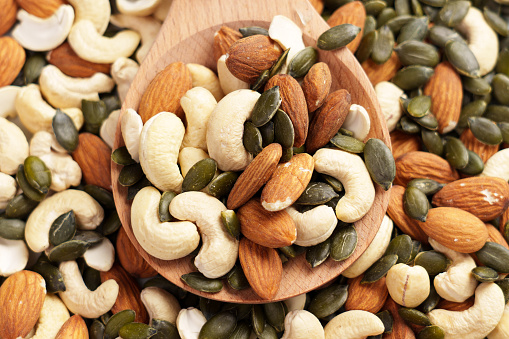 Nuts with pumpkin seeds in woodenware. Various mixed ingredients. Green dry kernels on a wooden rustic spoon with almonds and cashews