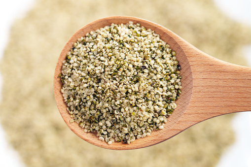 Shelled Hemp seeds in wooden spoon. Culinary superfood supplement. Peeled Cannabis grains close up. Health food ingredients