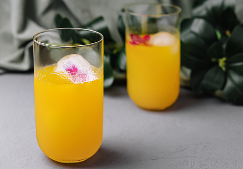 Elegant orange drinks with edible flowers in ice, perfect for summer events