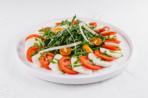 Vibrant caprese salad with tomatoes, mozzarella, arugula, and pesto drizzle on a white background