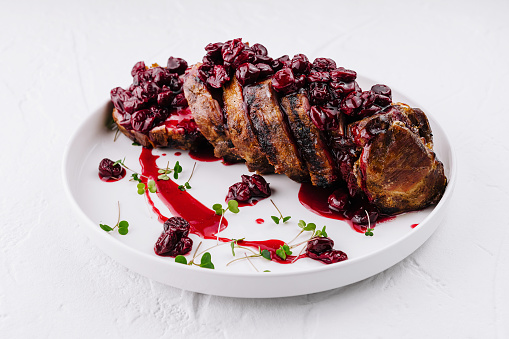 Juicy pork tenderloin topped with a rich cherry sauce, garnished with herbs on a white plate