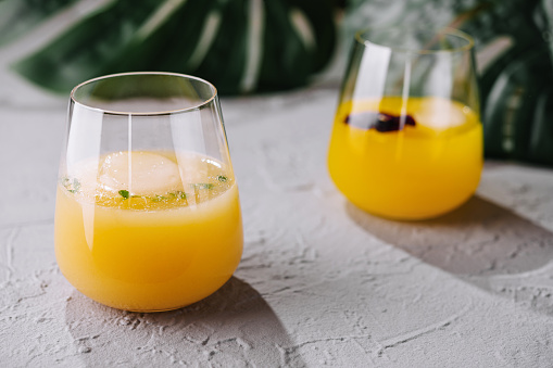 Two stemless glasses filled with vibrant orange juice and ice, garnished with berries, on a textured surface