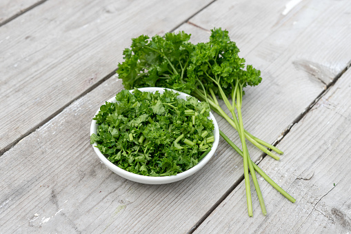 Bunch and sliced ​​fresh curly parsley on a light wooden background