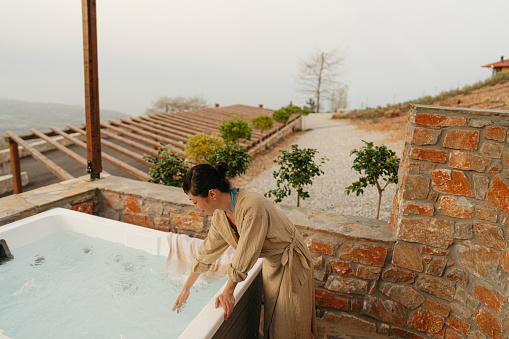 Photo of a mid adult Japanese woman getting ready to hop in a jacuzzi hot tub, located on a slopes of a mountain village