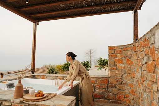 Photo of a mid adult Japanese woman getting ready to hop in a hot tub hot tub, located on a slopes of a mountain village