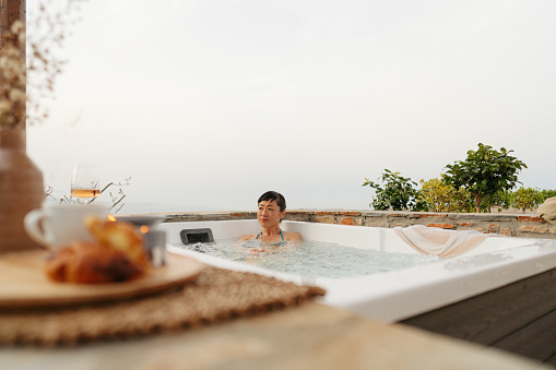 Photo of a mid adult Japanese woman soaking in a hot tub hot tub, located on a slopes of a mountain village