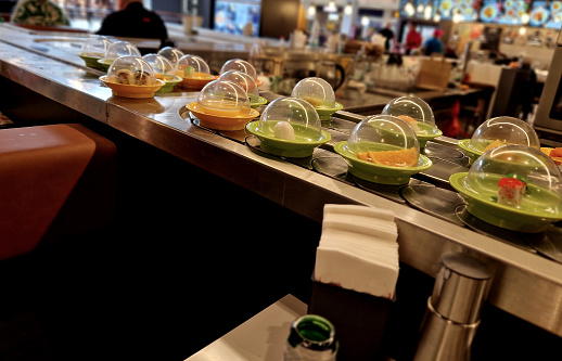 or sushi on the conveyor belt of taste of Japanese specialties. plates with sushi, maki, dim-sun and other Japanese, Chinese - simply East Asian specialties are constantly appearing on revolving belt