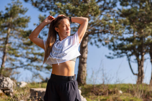 Young adult woman taking a break during trail running. She enjoys the relaxation after exercise outdoors with pine trees in the background.