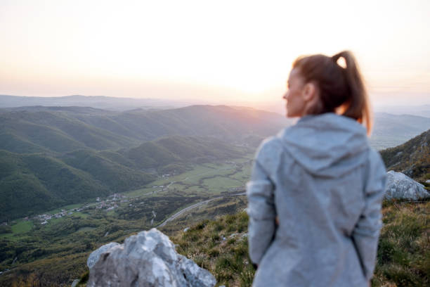 A young adult woman in contemplation, appreciating the vast mountainous landscape at sunset, embodying peace and relaxation.