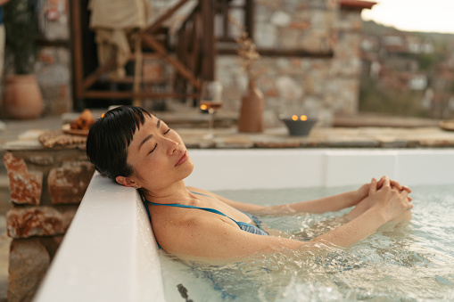 Photo of a mid adult Japanese woman soaking in a jacuzzi hot tub, located on a slopes of a mountain village