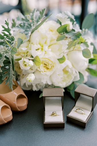 Wedding rings in boxes stand near the bride shoes and a bouquet of flowers on the table. High quality photo