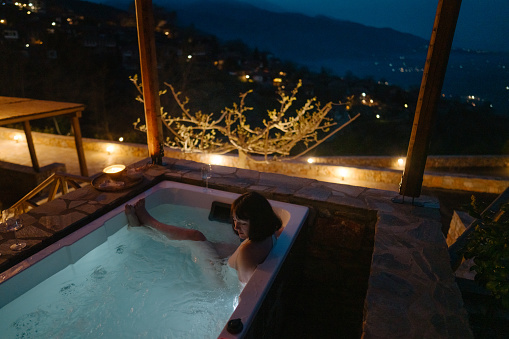 Photo of a young woman soaking in a hot tub hot tub, located on a slopes of a mountain village