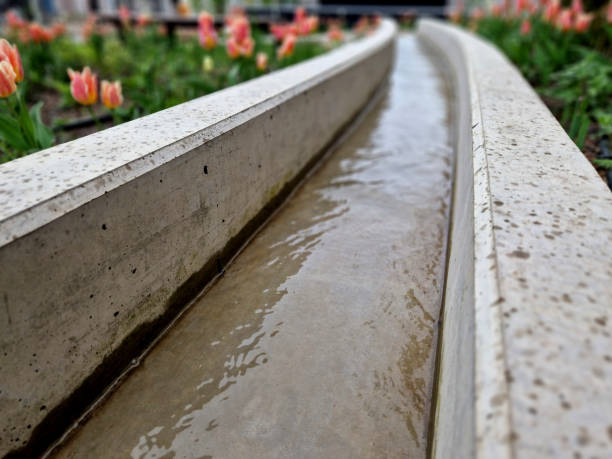 concrete gutter irrigation overhead channel. flower beds around concrete casting with a stream. orange tulips in the park. dripline, drainge