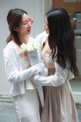 An intimate photo of two women in an emotional embrace, one with a bouquet of flowers.