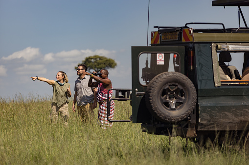 Couple of tourists and their guide looking in the distance in search of wild animals in nature reserve of Kenya.