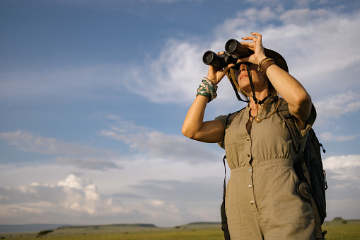 Low angle view of carefree female tourist looking through binoculars in wildlife reserve.