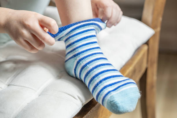close-up of female 4-year-old child, Preschooler learning to dress independently, putting on striped sock, Young kid achieving self-dressing milestones, Fine motor development, Self-care skills primer plano de una niña de 4 años, un niño en edad preescolar que aprende a vestirse de forma independiente, que se pone un calcetín a rayas, un niño pequeño que logra los hitos de vestirse solo, desarrollo de la motricidad fina, habilidades de auto