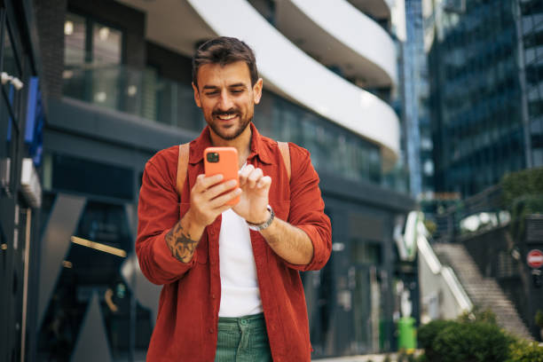 istock Relaxed man walking down the street and smiling using his phone to write a message. 2148956181