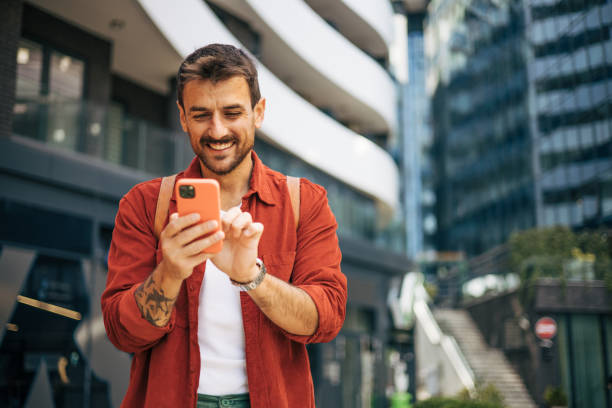 istock Relaxed man walking down the street and smiling using his phone to write a message. 2148956284