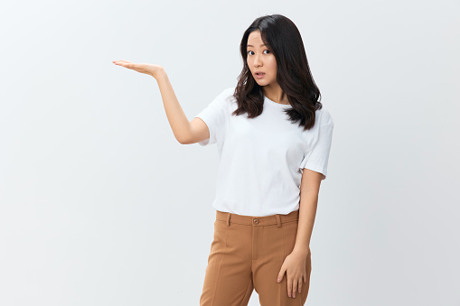 Hey, look here. Shocked Asian Korean young female in white basic t-shirt hold palms up show free place posing isolated on white studio background. The best offer for ad. People Lifestyle concept