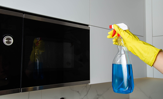 Anti-grease spray in the hand of a girl who is cleaning the kitchen. Cleaning the microwave oven from grease and dirt. Modern antistatic agent.