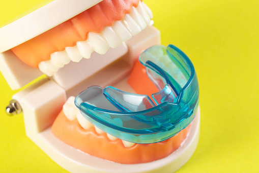 Therapeutic mouthguard on the background of a dental jaw mockup on a yellow background. Treatment of teeth grinding, bruxism in children and adults. Protecting tooth enamel from abrasion when grinding teeth.