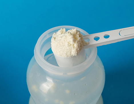 Preparation of baby milk food for feeding babies. Powdered milk mixture with vitamins and minerals on a blue background. Copy space for text