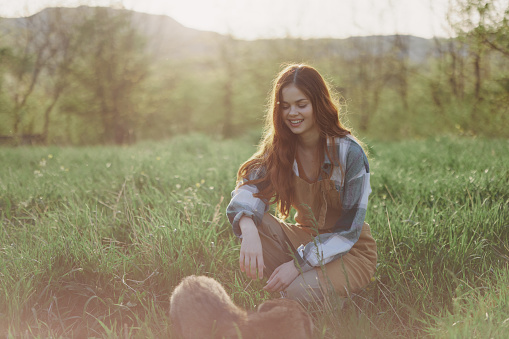 Young redheaded woman playing in nature with her dog in sunny park at sunset in summer. High quality photo