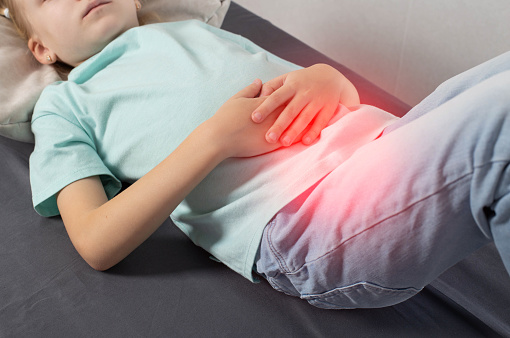 A seven-year-old girl in a green T-shirt lies and holds her sore stomach with her hands. Concept of appendicitis in children, inflammation in the epigastrium. Vomiting and nausea, redness