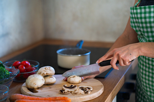 Close-up of unrecognizable woman cutting mushrooms in the kitchen