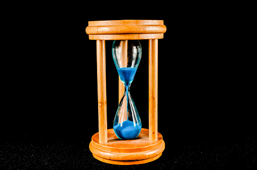 A wooden clock with a blue face and sand inside. The sand is almost gone, and the clock is set to the time of 3:00