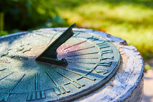 Sundial in Muncie conservatory garden, Indiana, displaying time amidst dappled sunlight and morning dew, hinting at antiquity and the tranquil passing of the day.